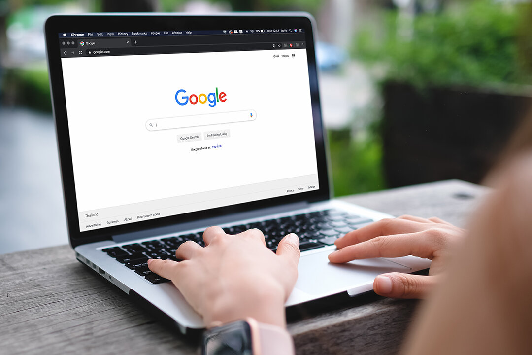 Hände auf Laptop-Tastatur mit geöffneter Google-Suchmaschine auf dem Bildschirm