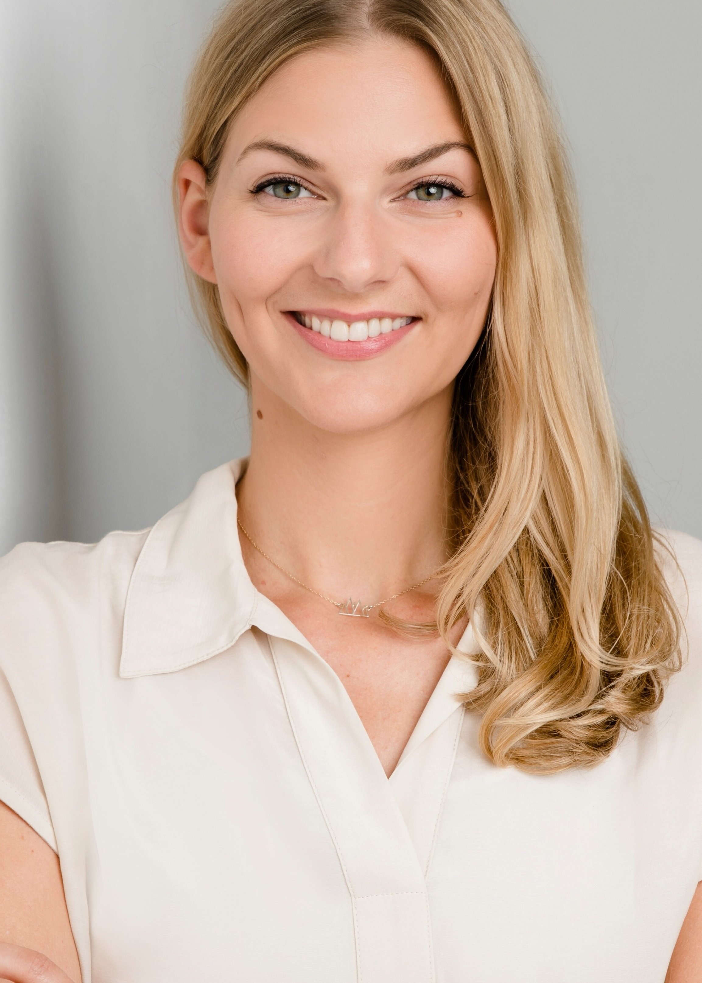 Kathi Moldan, Redakteurin, Porträt mit warmem Lächeln und direktem Blick – schulterlange honigblonde Haare mit Wellen, grün-haselnussbraune Augen, cremefarbene Bluse mit Kragen, delikate Halskette, vertrauenswürdig und nahbar, Expertise und Authentizität