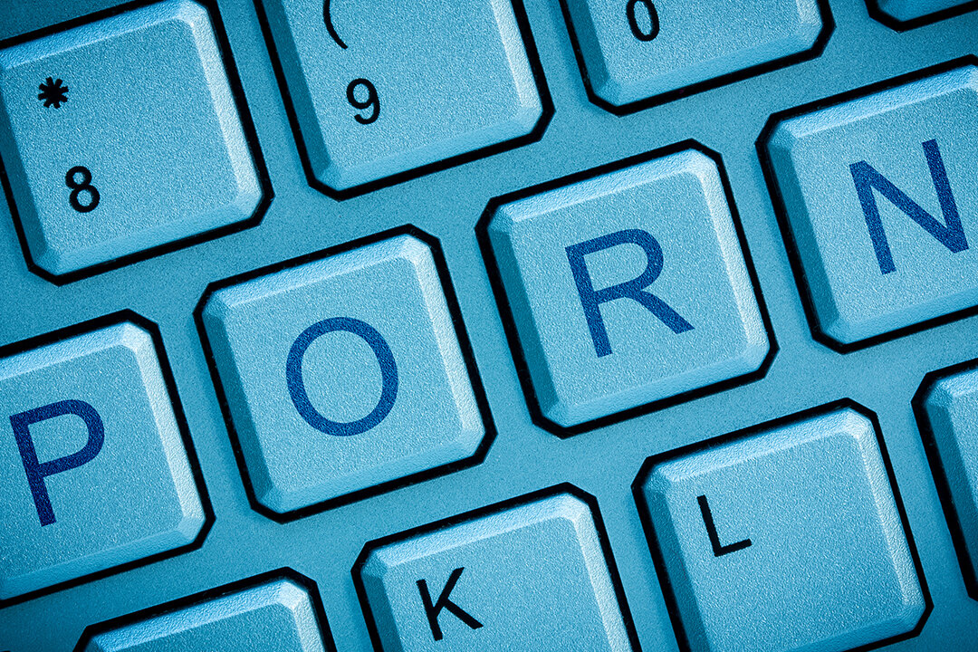 PORN-Schriftzug auf einer Computer-Tastatur in blauem Licht dargestellt.