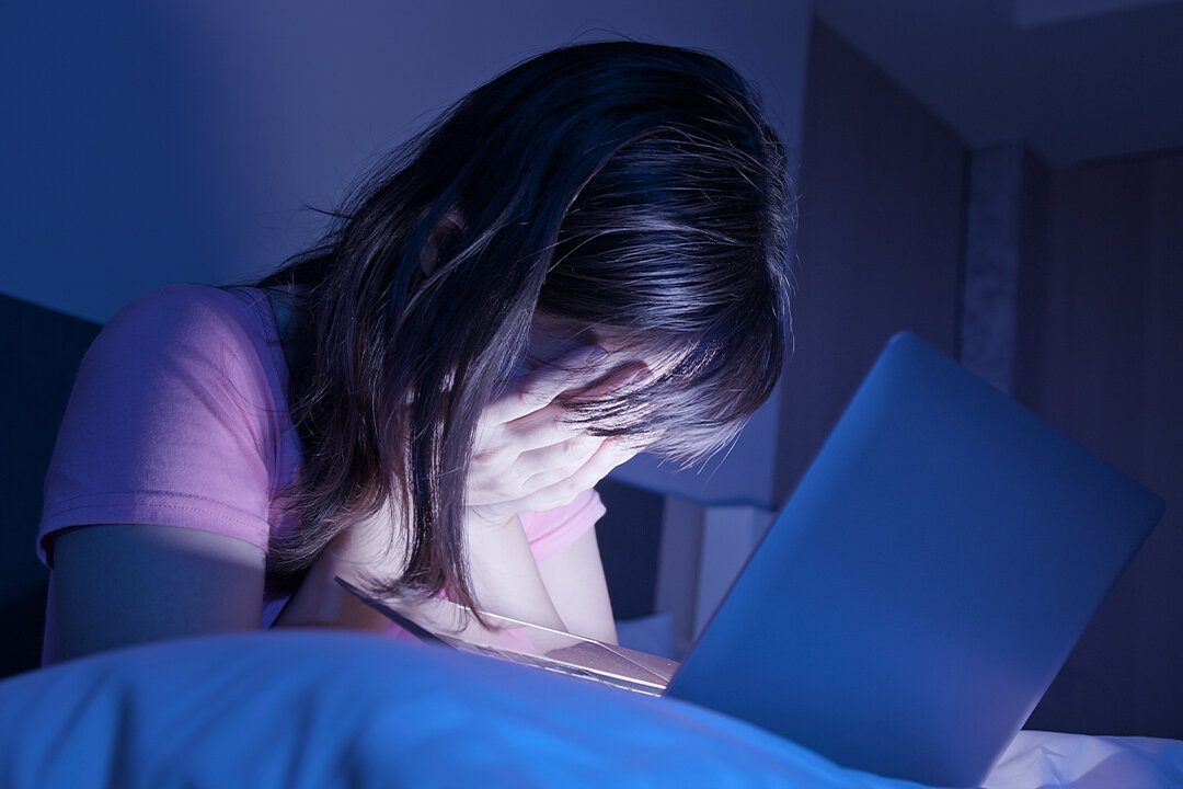 Jugendliche sitzt nachts vor einem Laptop und hält verzweifelt den Kopf in den Händen.