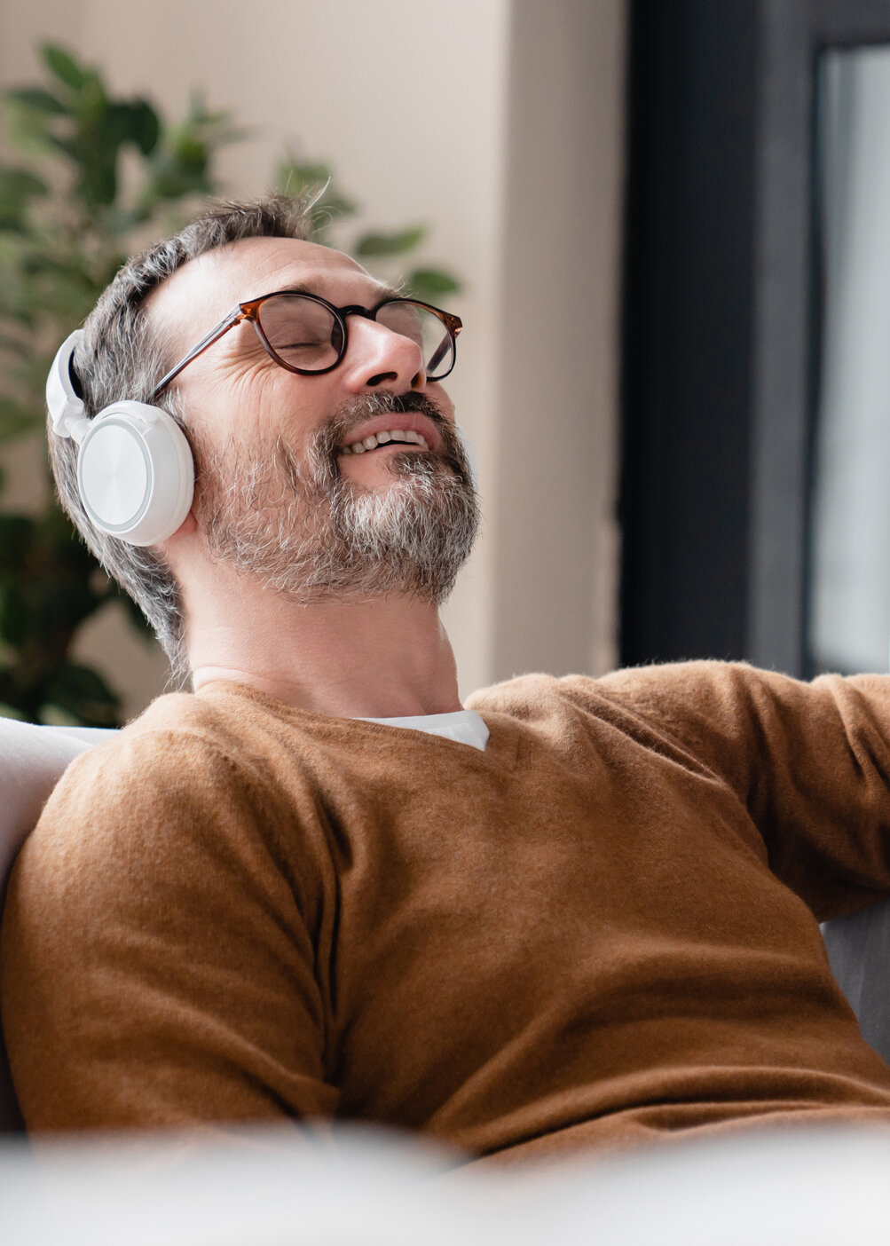 Entspannter Mann mit Kopfhörern auf Sofa, 7Mind App Integration, Wellness-Moment