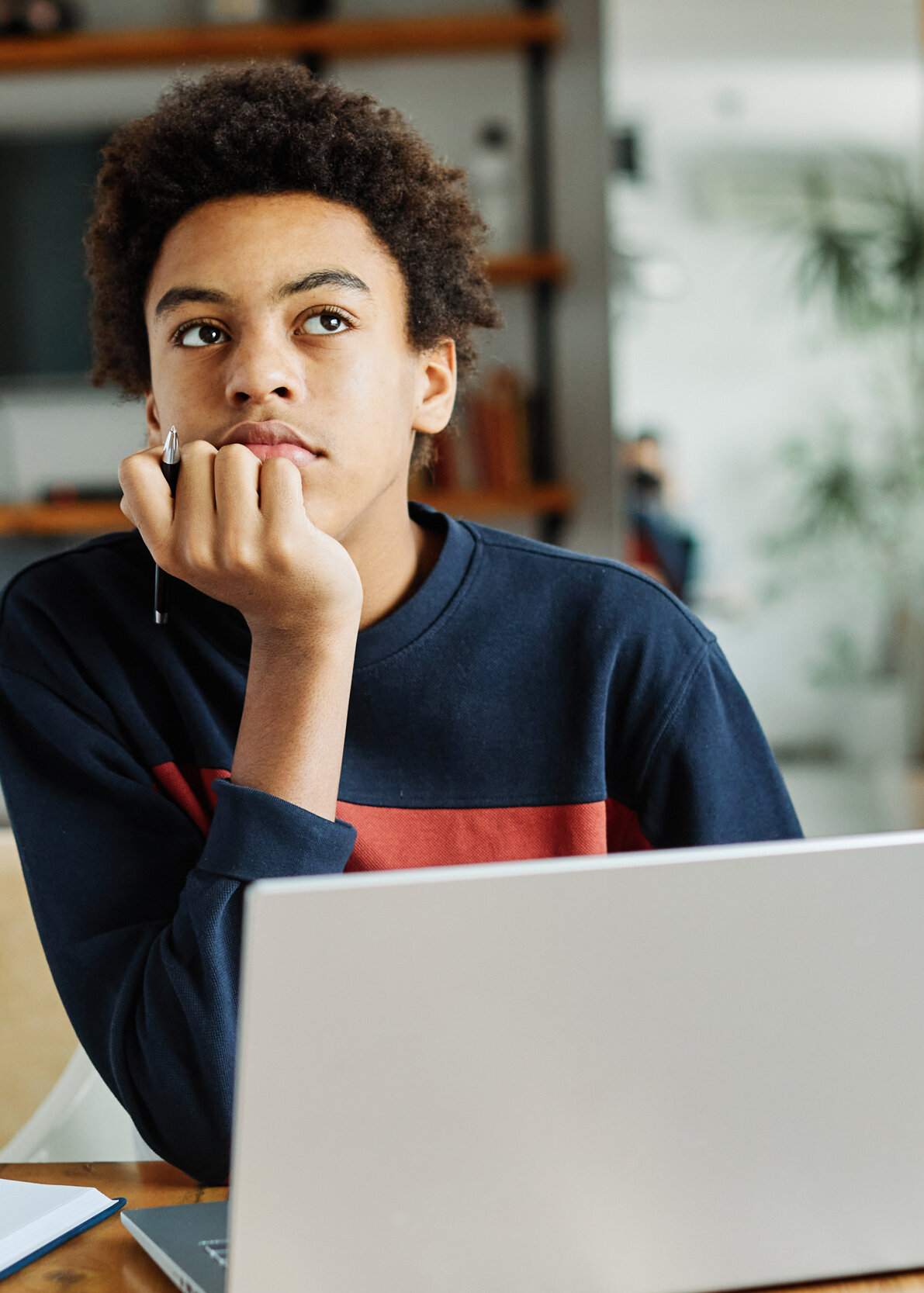  Nachdenklicher Schüler mit Laptop und Buch beim Wissencheck zuhause
