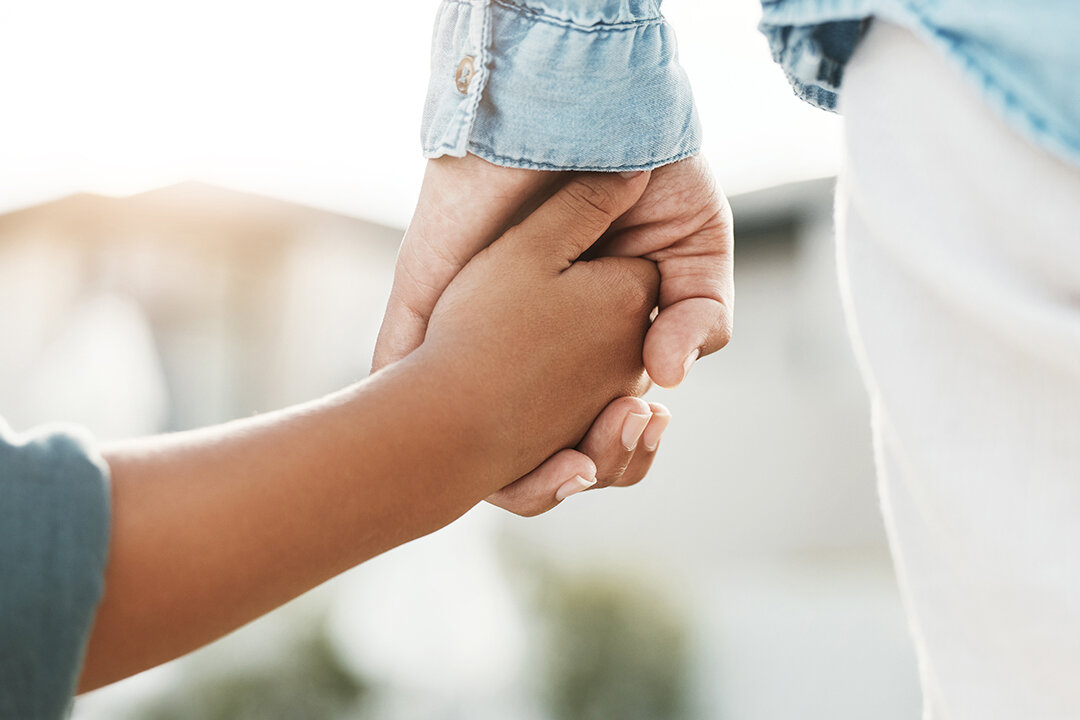 Nahaufnahme von zwei Händen, die sich halten: eine Erwachsenenhand und eine Kinderhand als Symbol für Geborgenheit und Vertrauen.