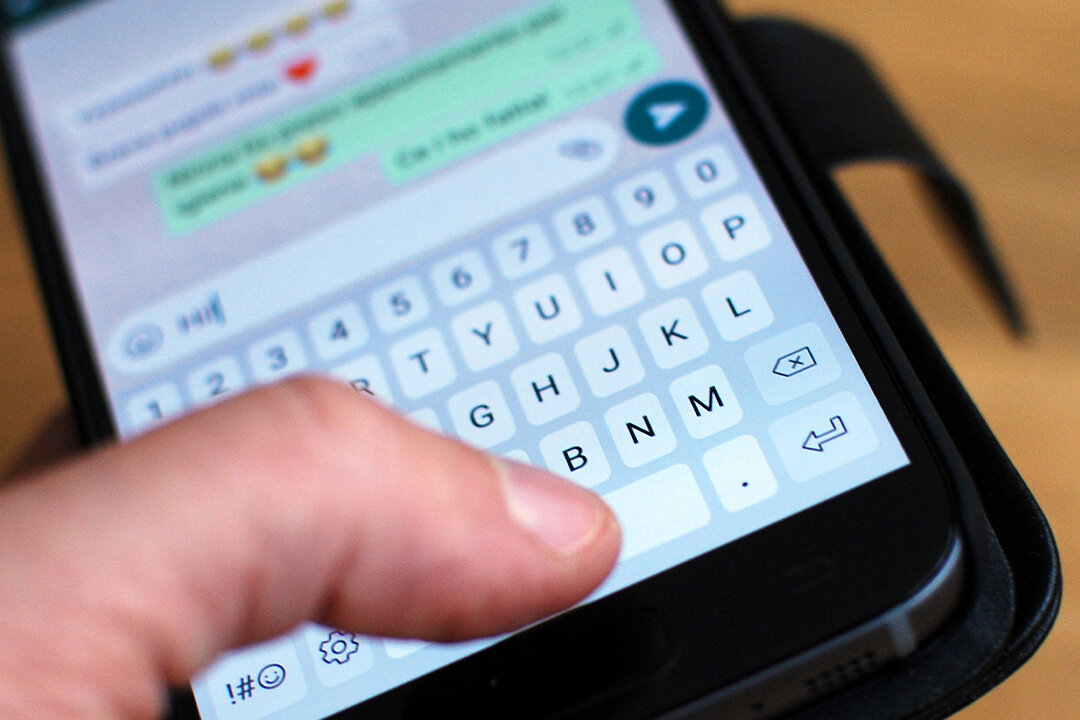 Hand hält ein Smartphone, auf dem ein geöffneter WhatsApp-Chat mit eingetippter Nachricht zu sehen ist.