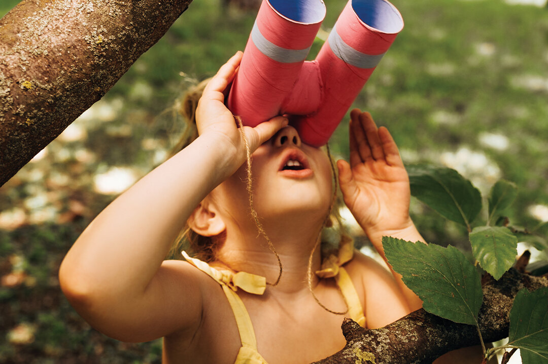 Kleines Mädchen schaut im Wald durch eine selbst gebastelte Papprohr-Fernglas in die Ferne