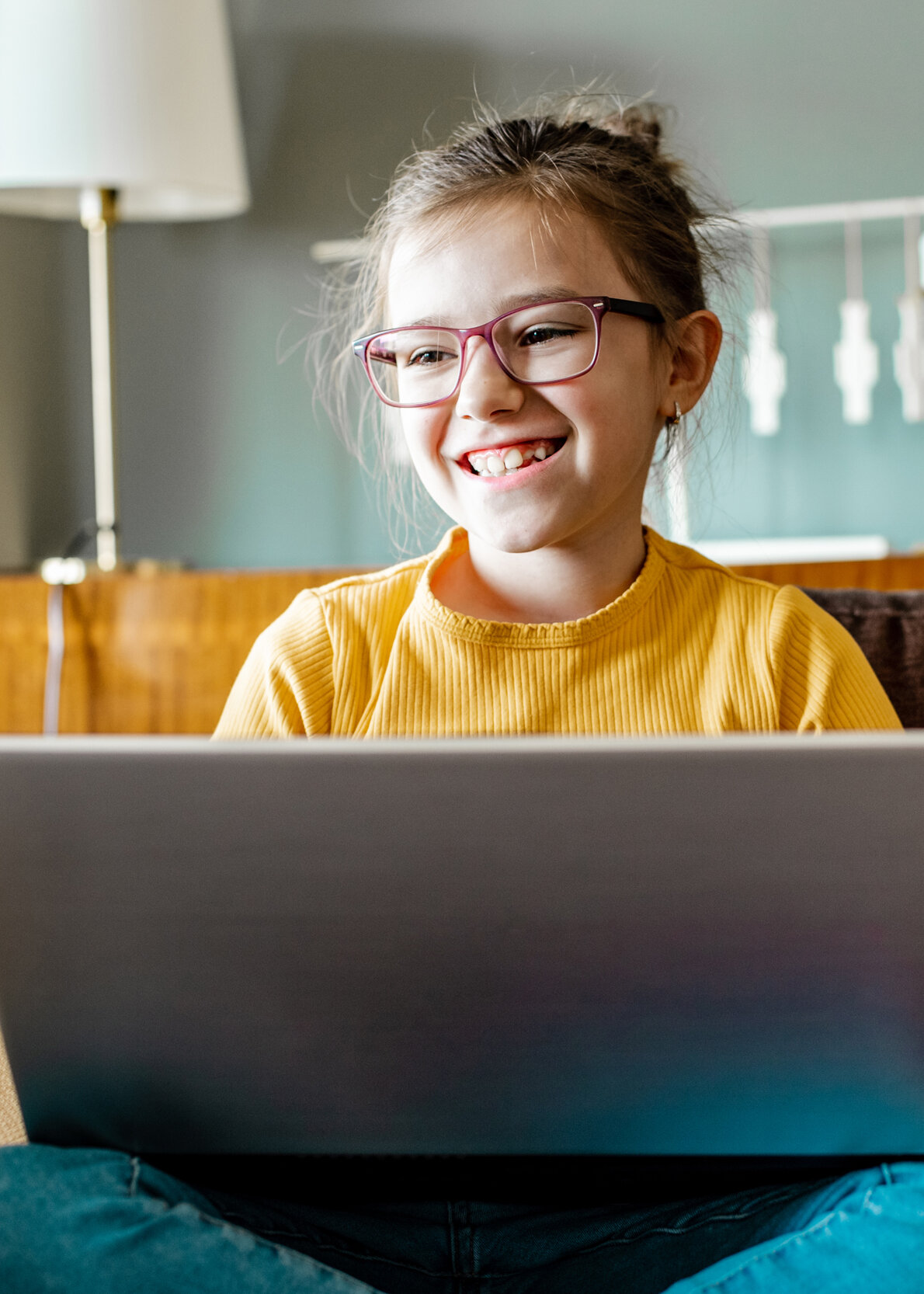 Schülerin mit rosafarbener Brille arbeitet konzentriert und lächelnd am Laptop auf Sofa