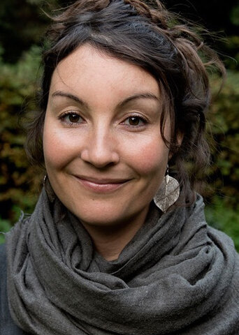 Anne Hackenberger, Redakteurin, Porträt mit warmem Lächeln, dunkle lockige Haare, grüner Hintergrund