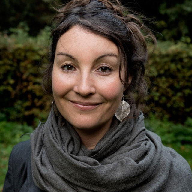 Anne Hackenberger, Redakteurin, Porträt mit warmem Lächeln, dunkle lockige Haare, grüner Hintergrund