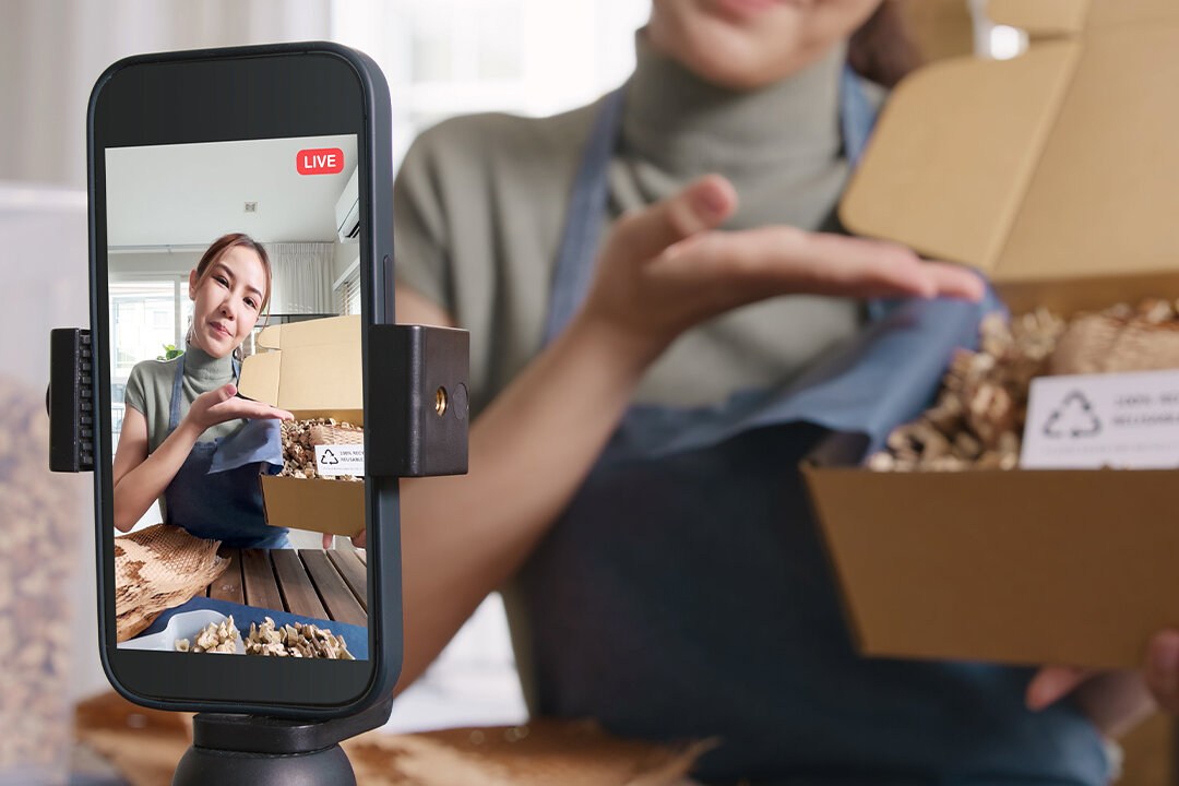 Mädchen präsentiert vor der Smartphone-Kamera einen offenen Karton mit umweltfreundlicher Verpackung.