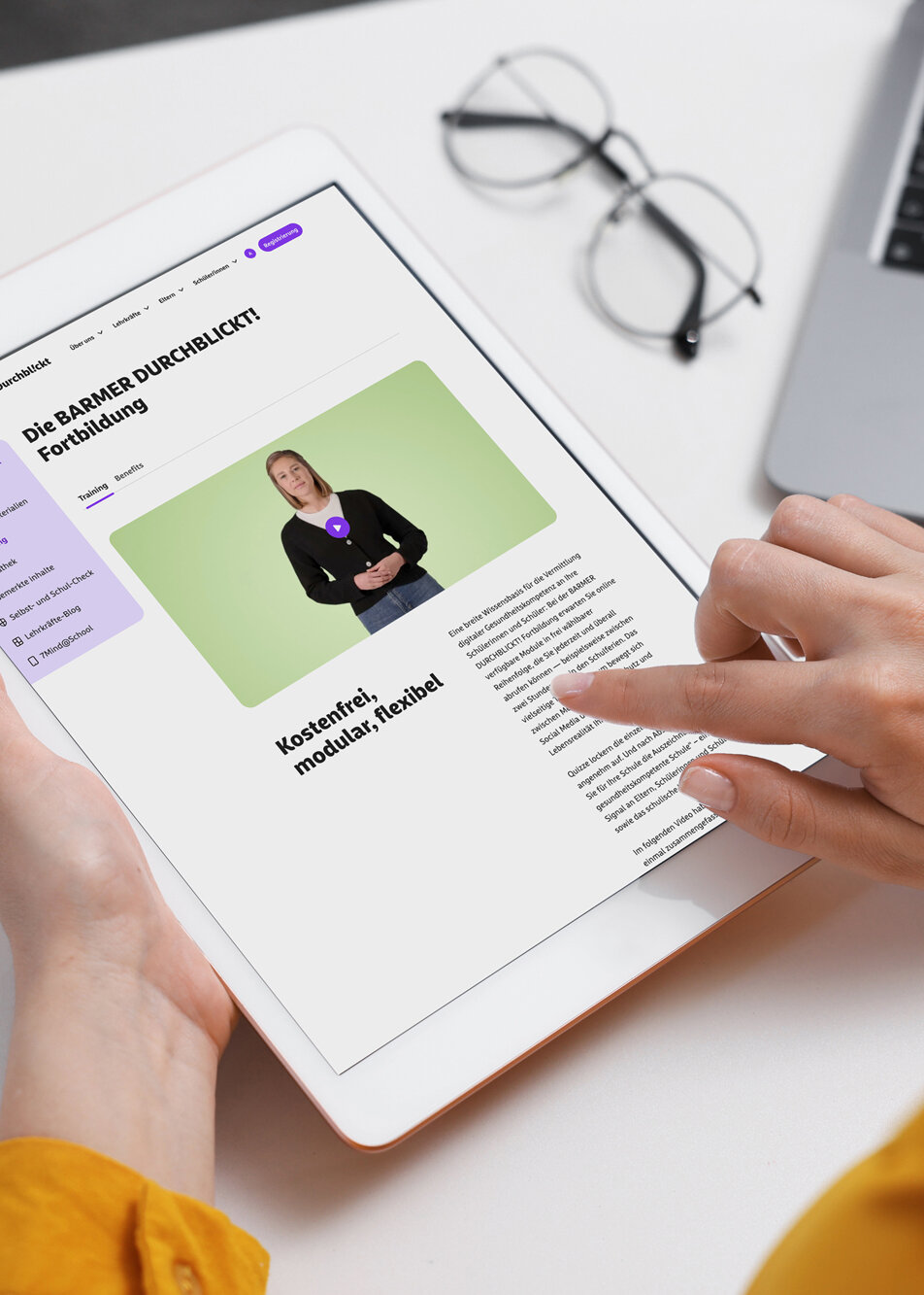 Mittelalte Lehrkraft mit dunkelbraunen Haaren in gelbem Pullover studiert konzentriert die BARMER Durchblickt Fortbildung auf Tablet am minimalistischen Schreibtisch – digitale Weiterbildung für Pädagogen