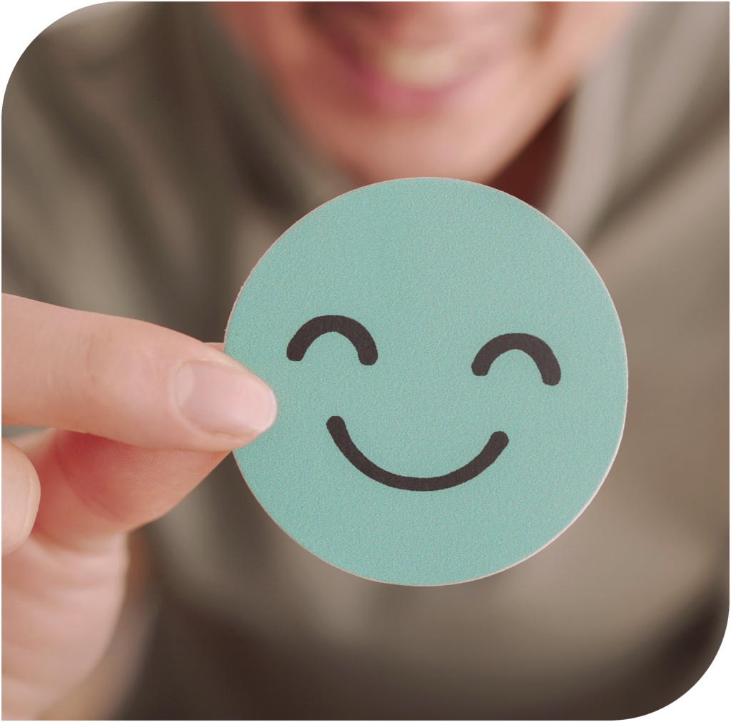 Hand hält einen lächelnden Smiley als Symbol für Wohlbefinden und mentale Gesundheit.