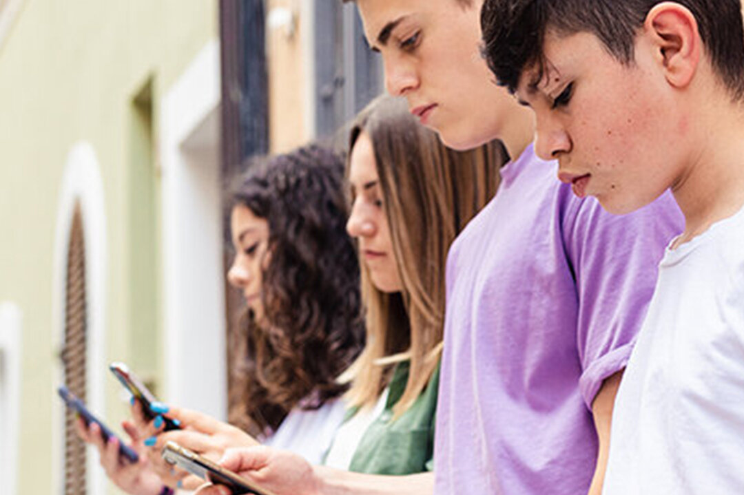 Vier Jugendliche lehnen mit Smartphones an Hauswand
