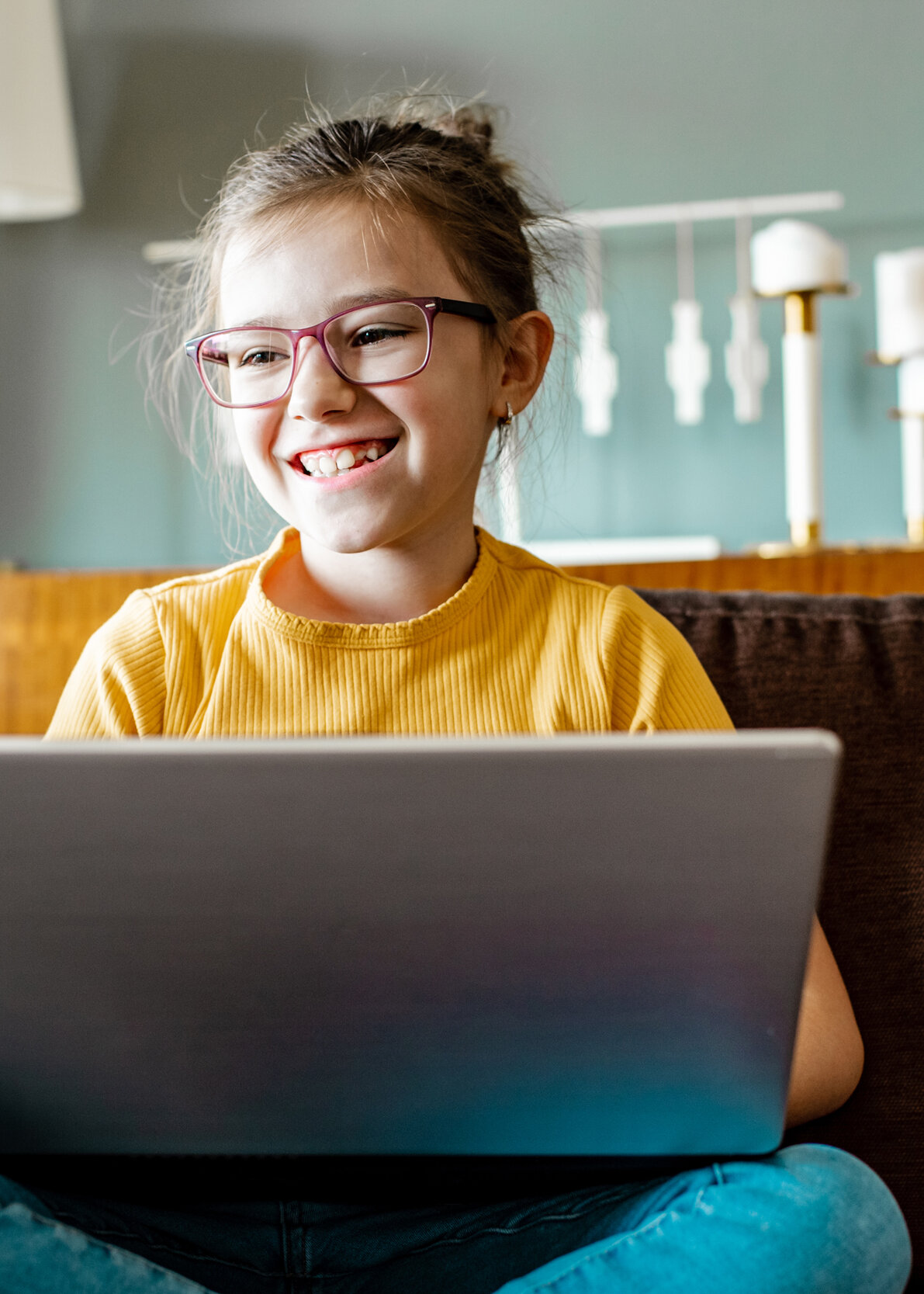  Lächelndes Mädchen mit Laptop auf dem Sofa beim digitalen Lernen