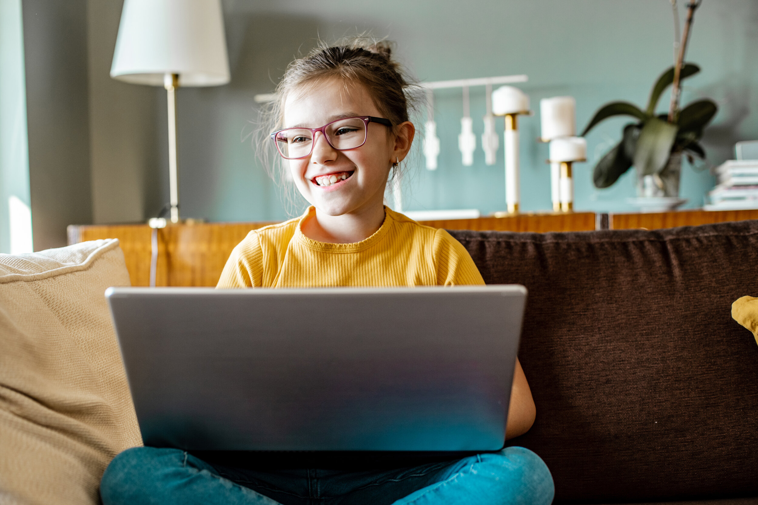 Lächelndes Mädchen mit Laptop auf dem Sofa beim digitalen Lernen