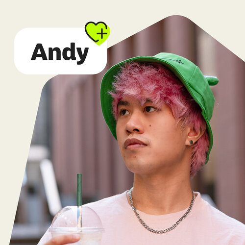 Porträt von Andy Lee mit pinken Haaren, grüner Fischerhut, hellrosa T-Shirt, Becher. Text „Andy“