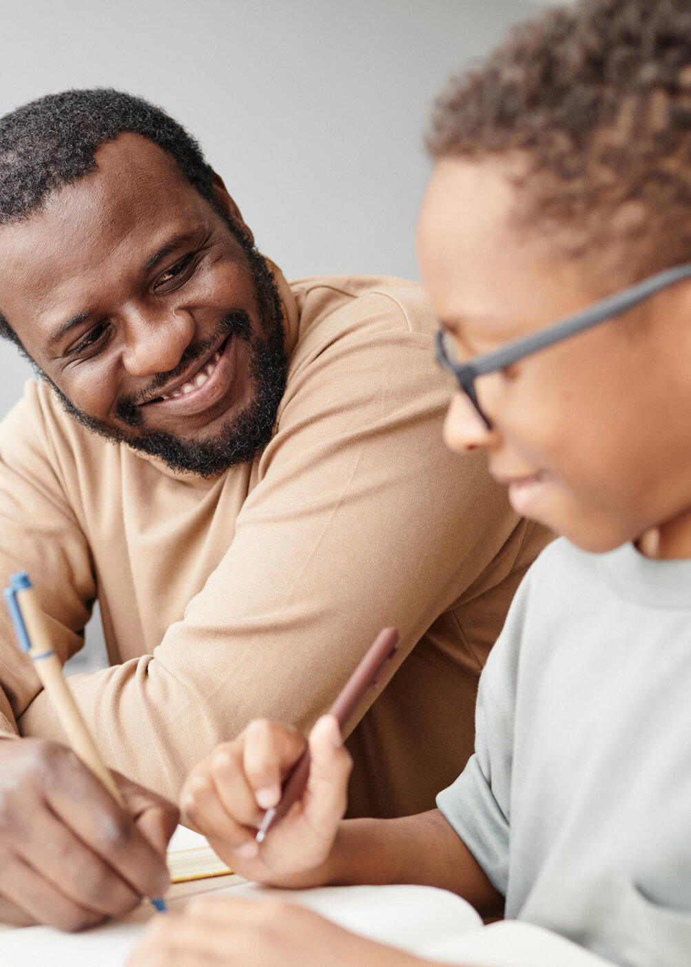 Vater und Kind mit Brille arbeiten gemeinsam am Laptop und mit Dokumenten – digitale Lernbegleitung, Eltern-Mentoring, Gesundheitskompetenz
