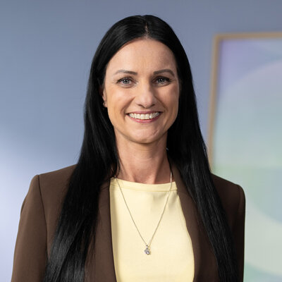 Kristin Van der Meer im braunen Blazer, gelbes Oberteil, Porträt vor hellem Hintergrund