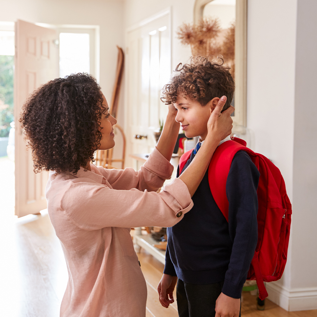 Mutter richtet ihrem Sohn mit Schulrucksack im Eingangsbereich liebevoll die Haare, bevor er das Haus verlässt. DGK_Artikel-05_Praise-Children.jpg