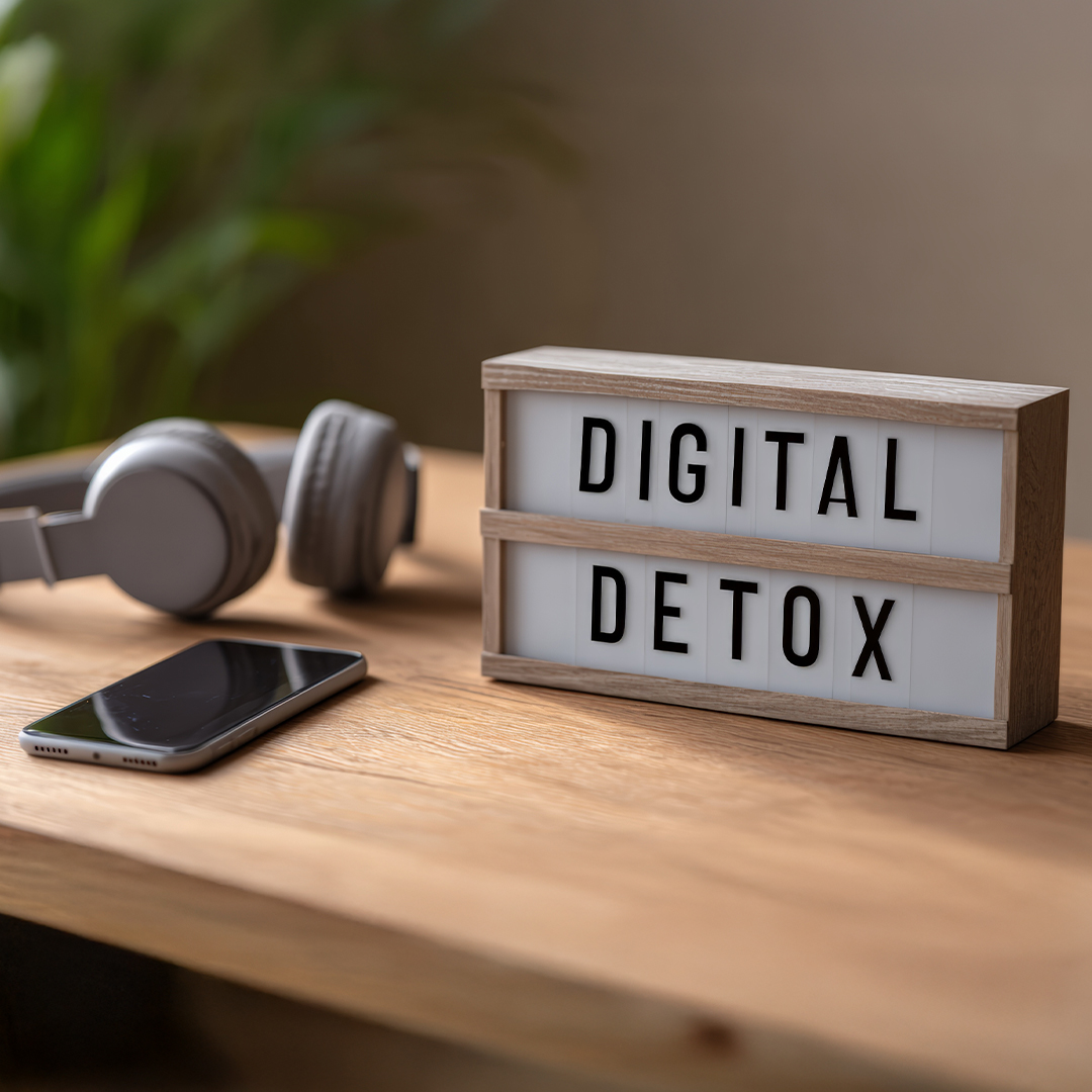Leuchtbox mit Aufschrift „Digital Detox" auf Holzoberfläche, daneben abgelegtes Smartphone und Kopfhörer – Symbol für digitale Auszeit im Familienalltag