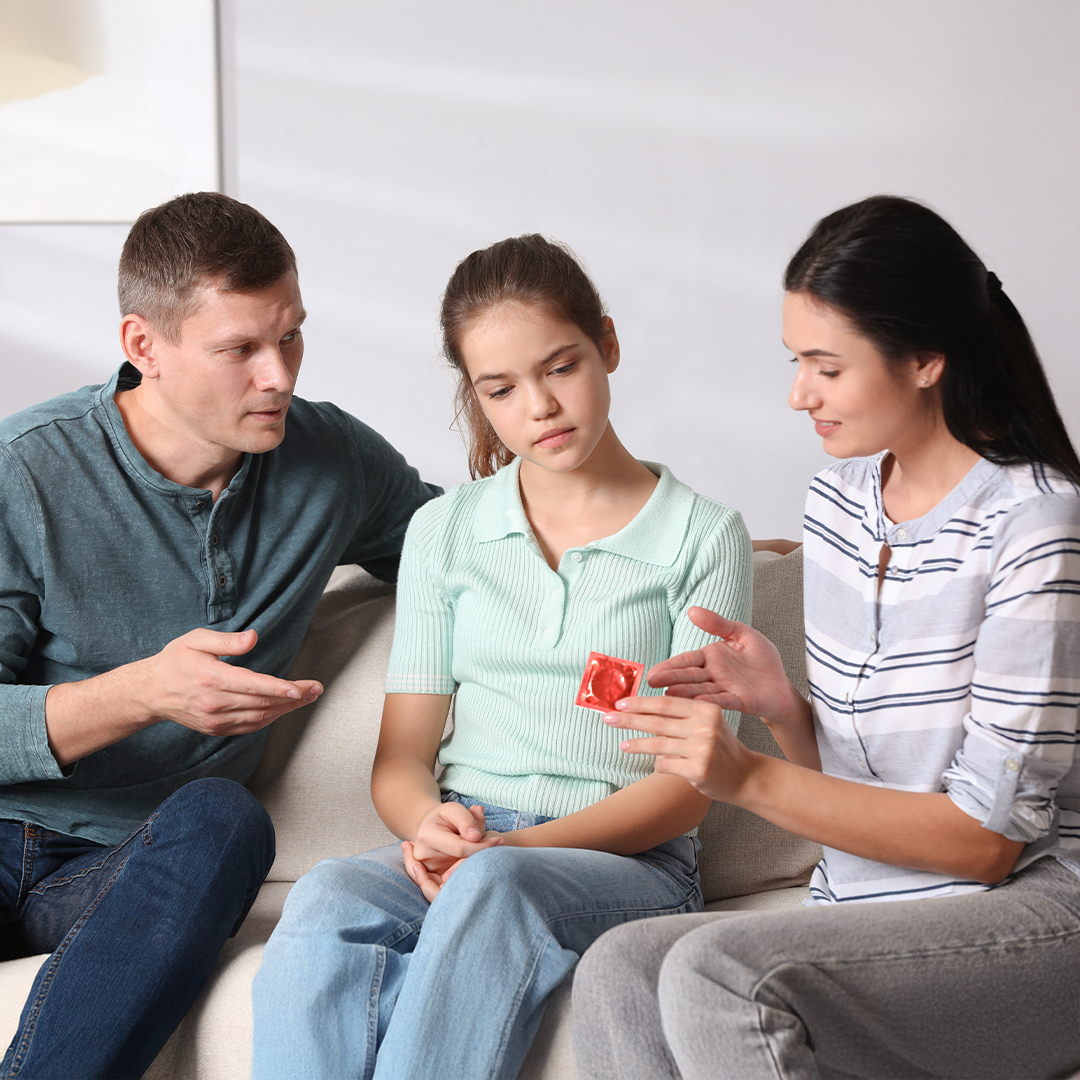 Zwei Erwachsene sprechen mit einem Mädchen auf dem Sofa und erklären ihr anhand eines Kondoms das Thema Verhütung 20251215_DGK_Artikel-13_Sex-Education-Tiktok.jpg