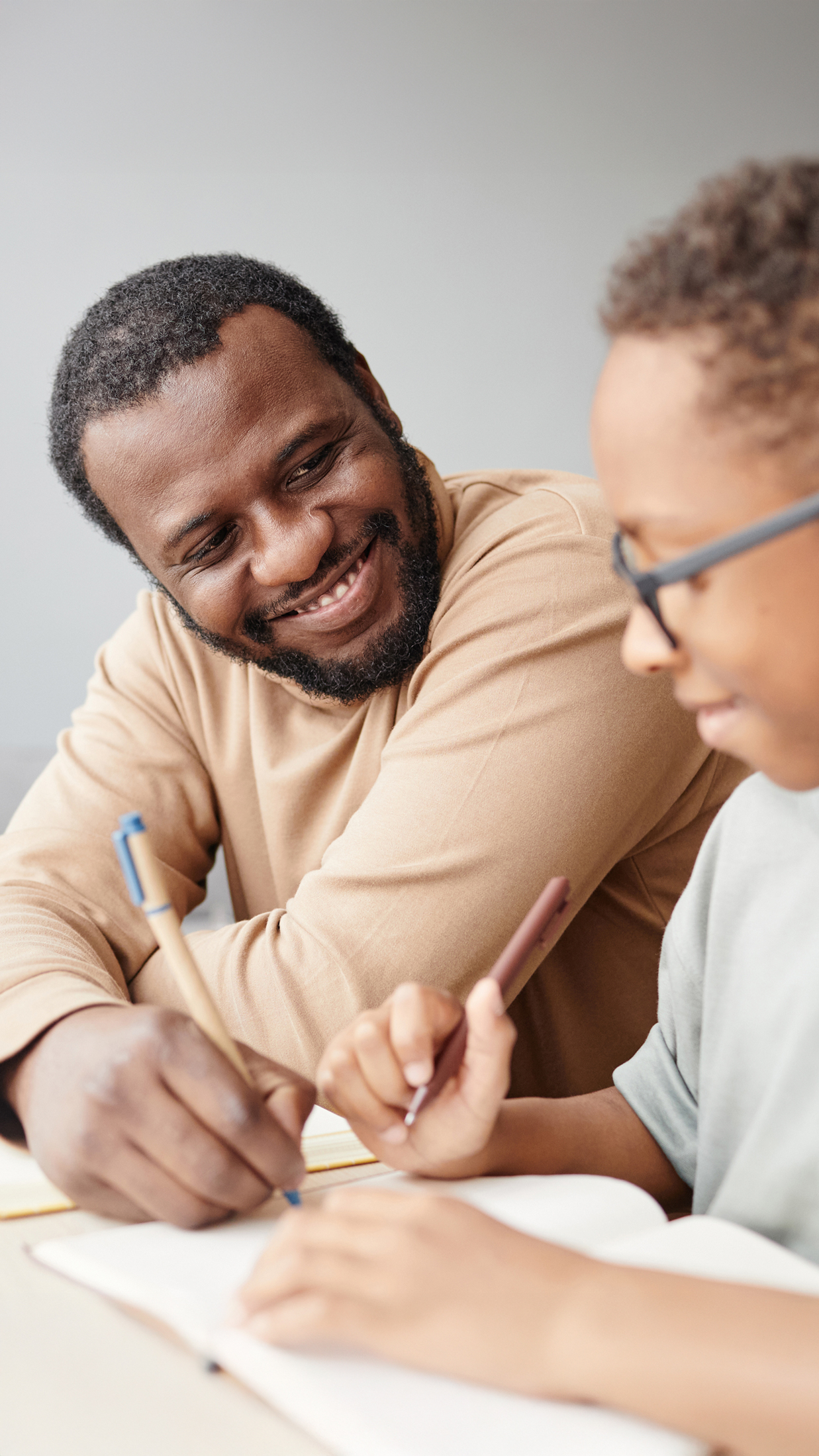 Vater und Kind mit Brille sitzen zusammen an Schreibtisch mit Dokumenten und blauem Stift – gemeinsames Lernen, Lernbegleitung, Mentoring