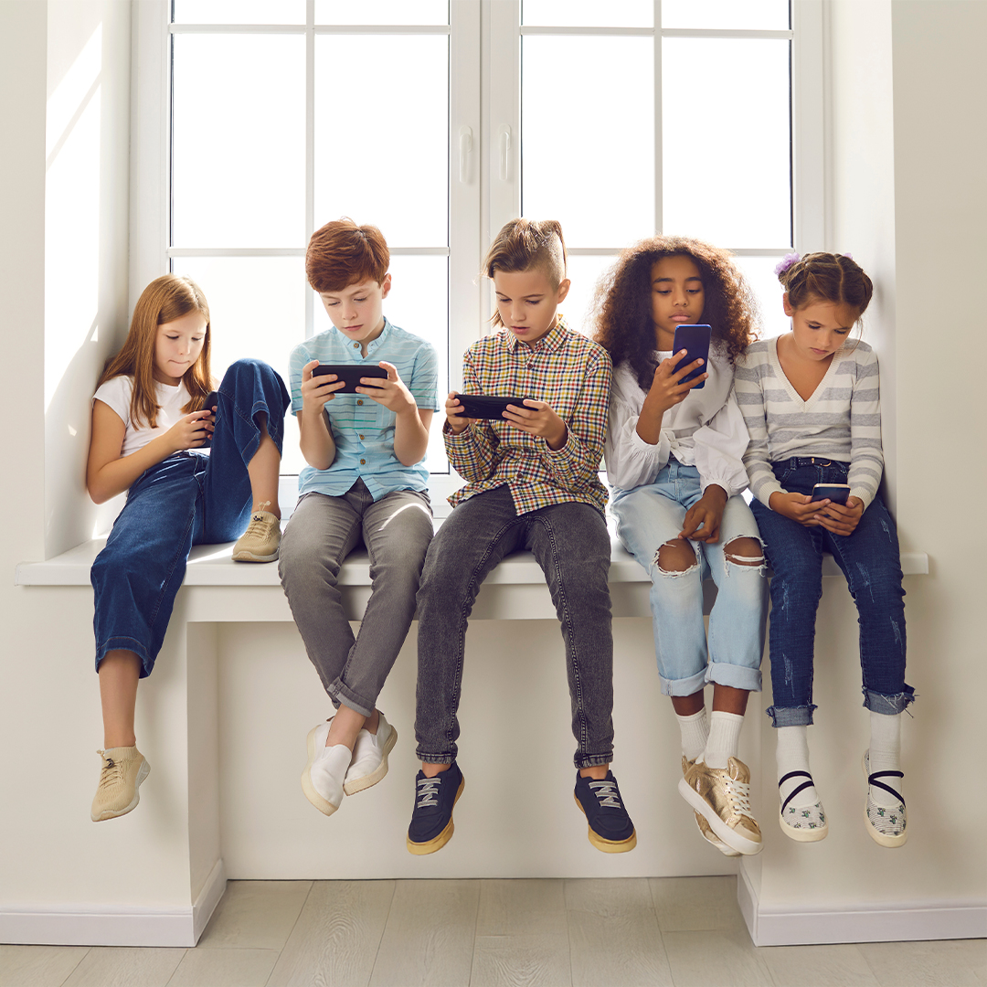 Fünf Kinder sitzen nebeneinander auf einer Fensterbank und schauen konzentriert auf ihre Smartphones. 20251215_DGK_Artikel-04.01_Class-Chats.jpg