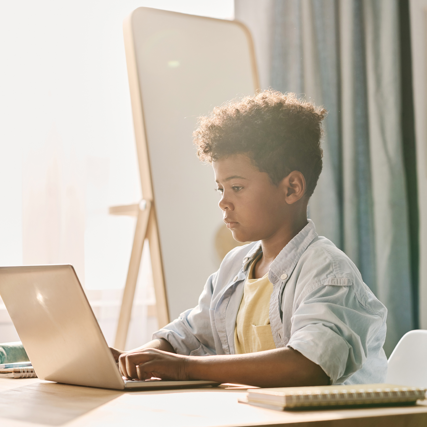 Schüler arbeitet konzentriert am Laptop, grüne Notizbücher auf Holztisch, produktiver Arbeitsplatz