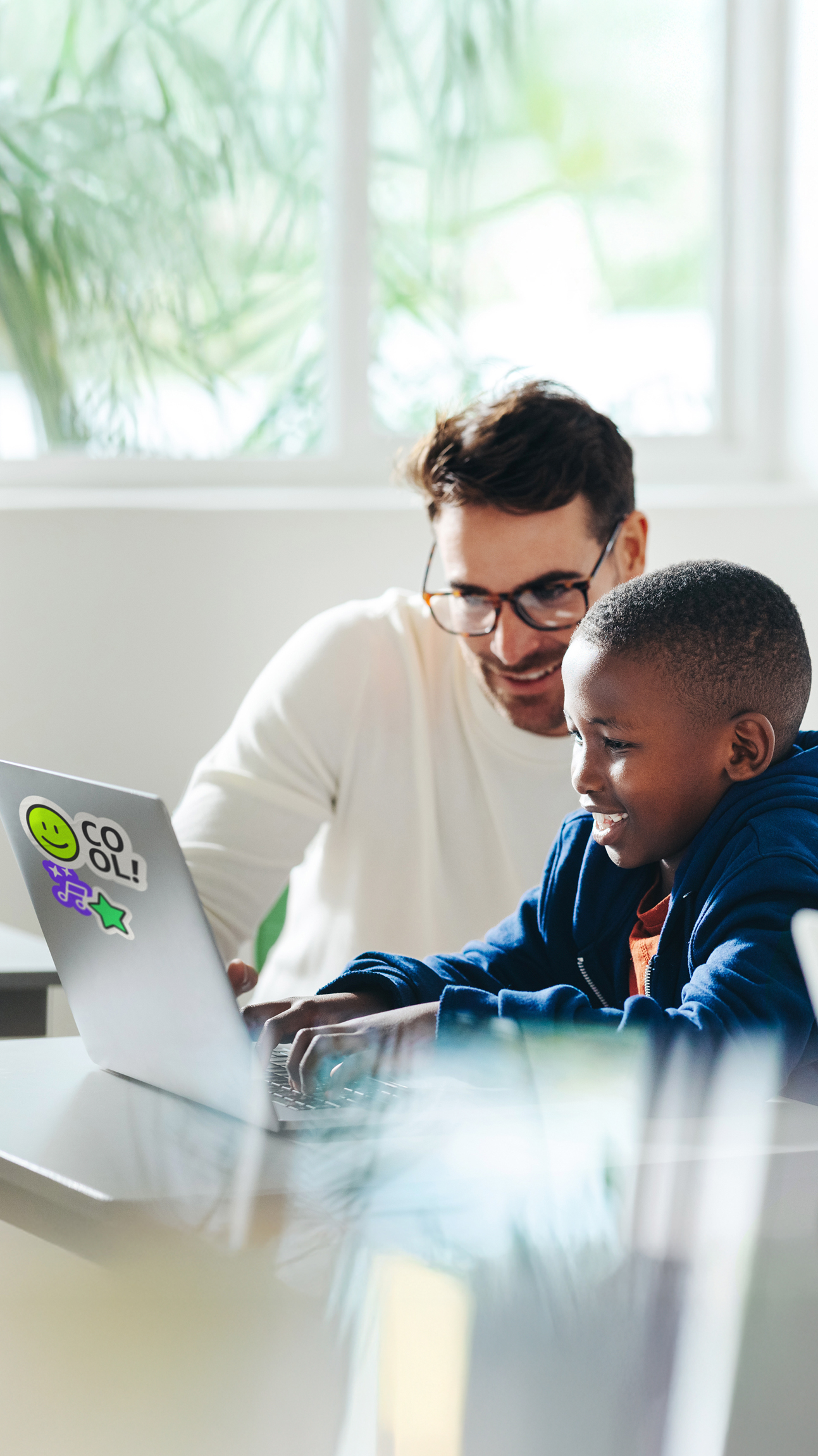 Vater unterstützt Kind am Laptop beim Erlernen digitaler Kompetenzen