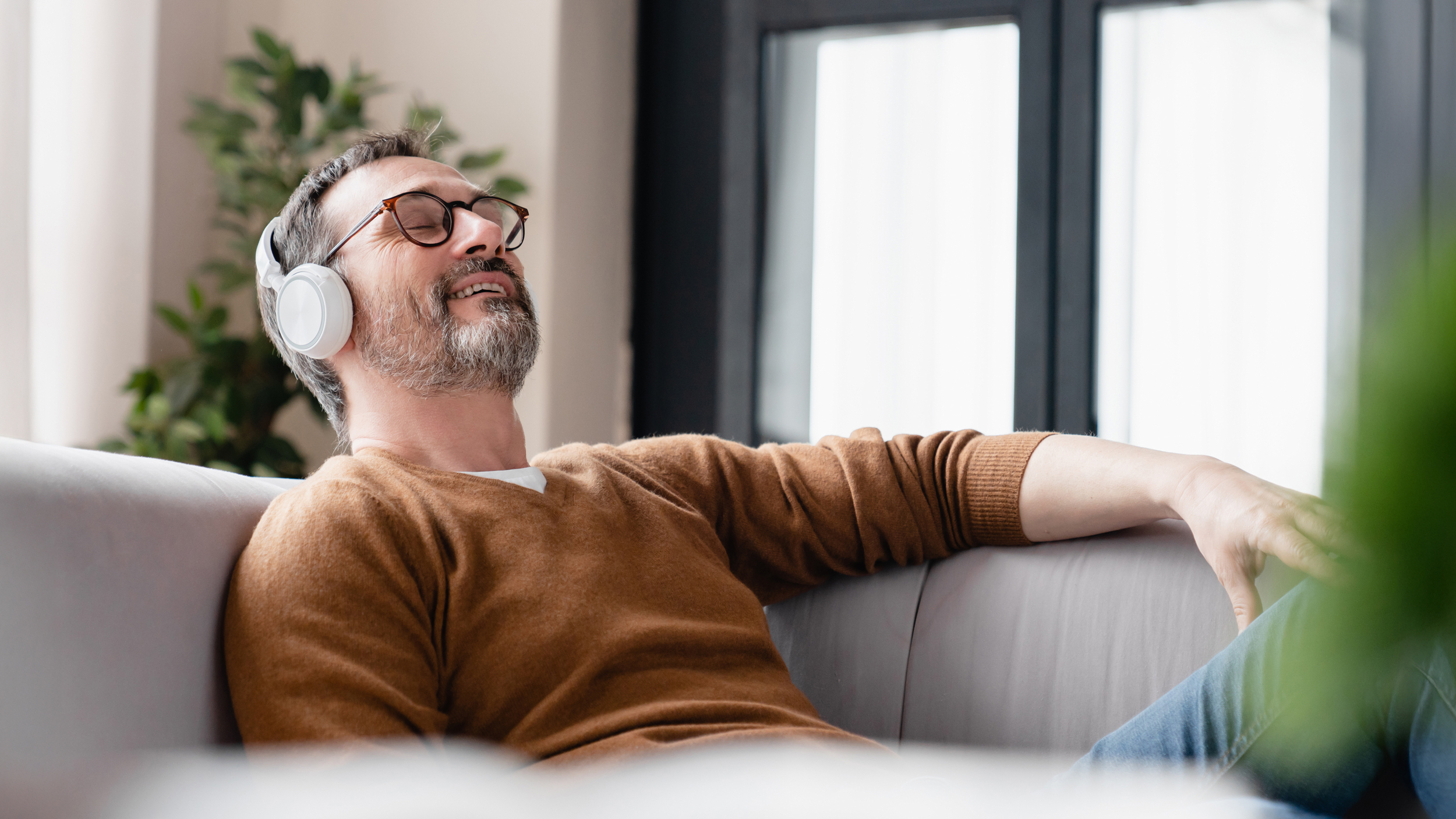 Entspannter Mann mit Kopfhörern auf Sofa, 7Mind App Integration, Wellness-Moment
